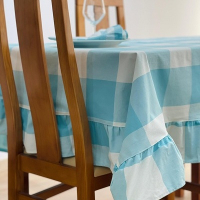Toalha de mesa xadrez azul claro e branco com babado em mesa com cadeiras de madeira