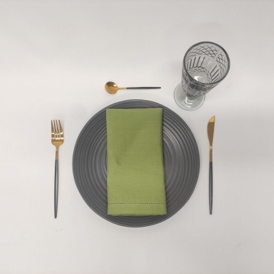 Conjunto de jantar com prato cinza escuro, guardanapo verde, talheres dourados e pretos e copo de vidro transparente com padrão
