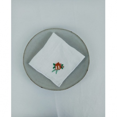 Guardanapo branco bordado com desenho de presente vermelho e raminho verde sobre prato cinzento