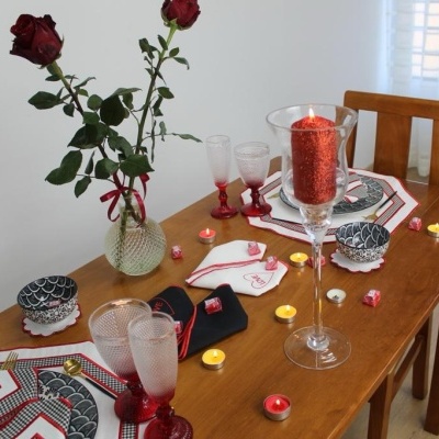 Mesa de madeira decorada com rosas vermelhas, velas e toalhas de mesa em tons de vermelho, branco e cinza