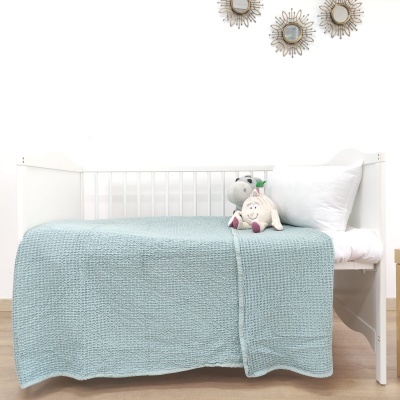 Cama branca de bebé com manta azul claro e dois peluches em cima, três espelhos redondos na parede branca