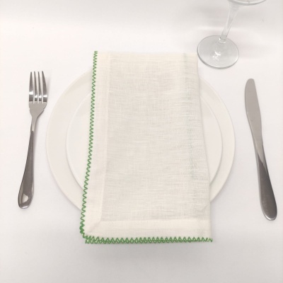 Mesa posta com prato branco, guardanapo branco com borda verde, talheres metálicos e taça de vidro
