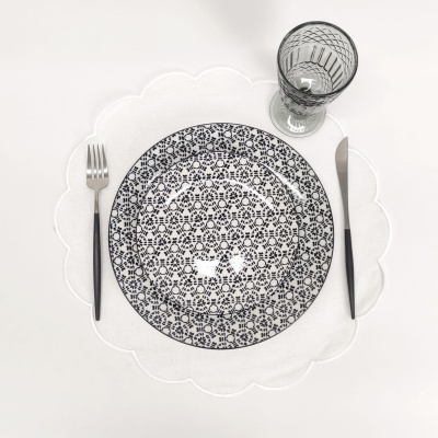 Conjunto de mesa com prato decorado, talheres pretos e copo de vidro sobre guardanapo branco