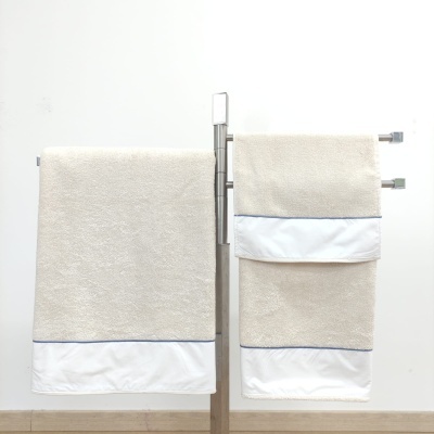 Conjunto de toalhas de banho bege com faixa branca satinada penduradas numa estrutura metálica