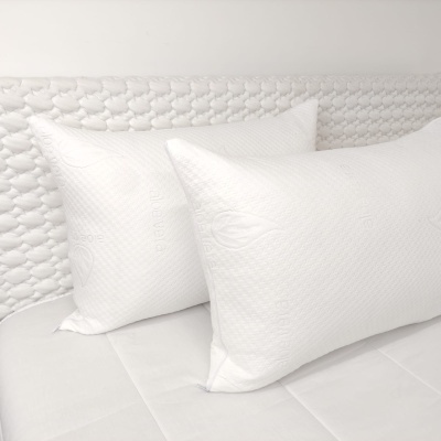 Duas almofadas brancas em cama com cabeceira estofada branca e padrão trançado