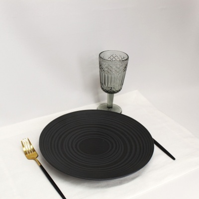 Conjunto de prato preto, talheres preto e dourado, copo cinzento em fundo branco