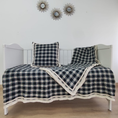 Cama de bebé branca com colcha e almofada xadrez azul, branco e bege com borda rendada.