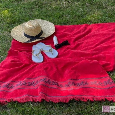 Toalha de praia vermelha com padrão cinza, chapéu de palha, chinelos brancos, frasco e óculos de sol