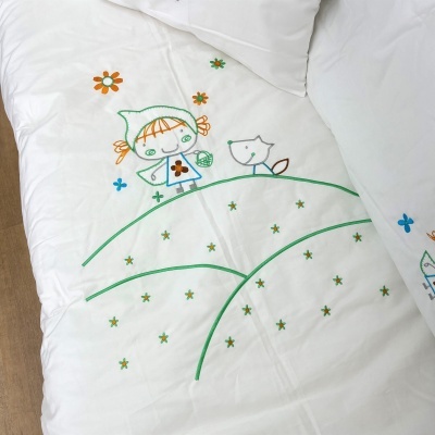 Colcha branca com desenho bordado de criança e gato sobre colinas verdes