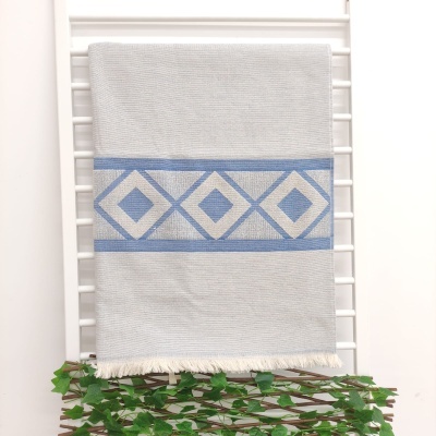 Toalha branca com padrão geométrico azul pendurada num suporte branco com folhas verdes em baixo