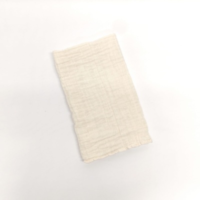 Toalha bege claro com textura suave e enrugada sobre superfície branca.