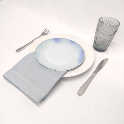 Conjunto de jantar com prato azul e branco, guardanapo cinzento, talheres prateados e copo de vidro transparente