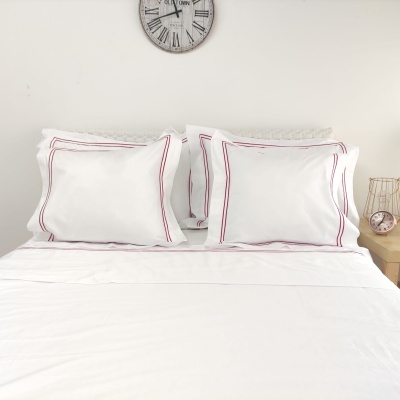 Conjunto de roupa de cama branca com fronhas com linhas vermelhas e relógios no fundo