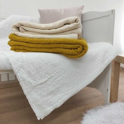 Cama com mantas branca, bege e mostarda e almofada rosa