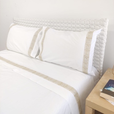 Lençóis brancos com bordados dourados geométricos em cama com cabeceira branca trançada