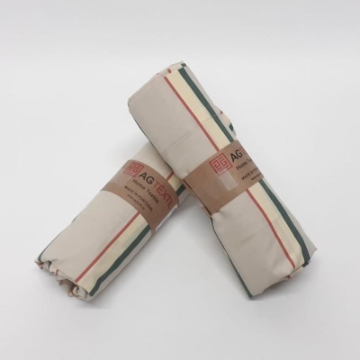 Dois rolos de tecido com padrão xadrez bege, verde e vermelho com etiqueta AG TEXTIL Home & Style