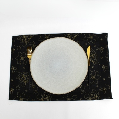 Prato cinzento com borda dourada, talheres dourados e guardanapo preto com padrão dourado