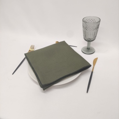 Conjunto de mesa com prato branco, guardanapo verde escuro, talheres preto e dourado, copo cinzento translúcido