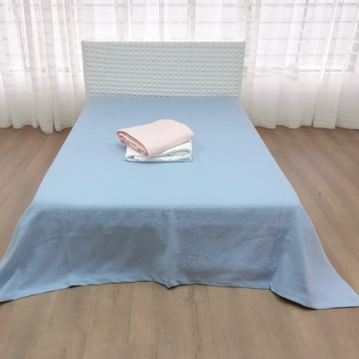 Cama com roupa de cama azul clara e tecidos cor-de-rosa e branco dobrados em cima, com cabeceira branca e cortinas ao fundo