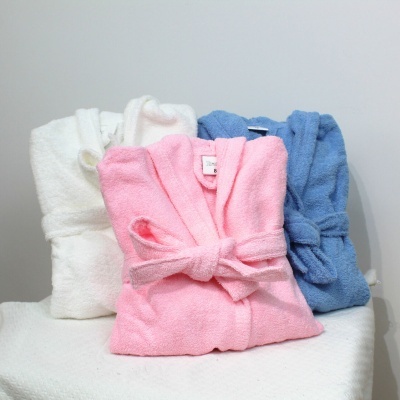 Robes de banho branco, rosa e azul dobrados com cintos amarrados sobre superfície branca