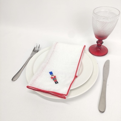 Conjunto de louça com prato branco, guardanapo decorado e copo vermelho texturizado, talheres ao lado