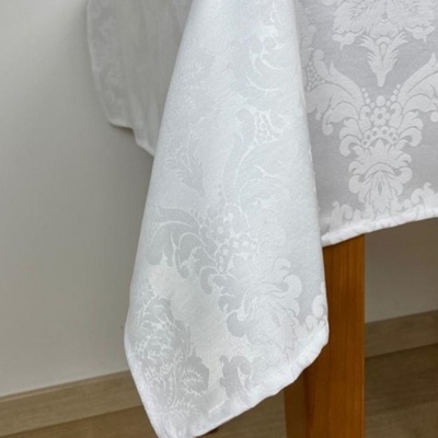 Toalha de mesa branca com padrão floral damascado em relevo numa mesa de madeira.