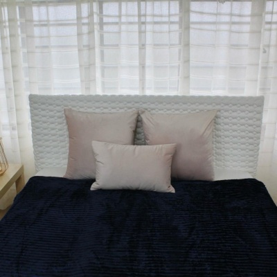 Cama com três almofadas bege claro e cobertor preto numa cabeça texturizada branca.