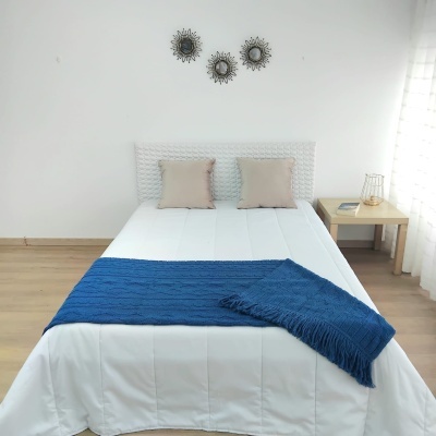 Cama arrumada com manta azul e almofadas bege em quarto minimalista branco