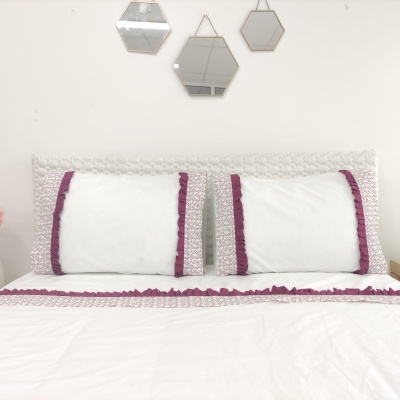 roupa de cama branca com franjas púrpura e espelhos hexagonais na parede