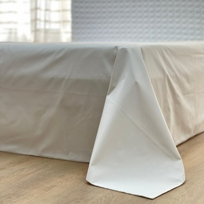 Capa de colchão branca em tecido liso sobre colchão com cabeceira texturizada branca.