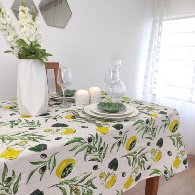 toalha de mesa branca com padrão de limões e ramos verdes, vaso branco com flores, velas, copos e pratos numa mesa de madeira
