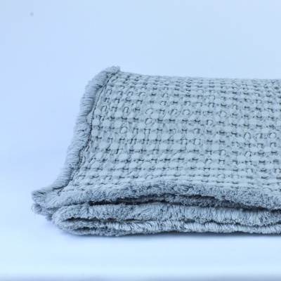 Manta cinza texturizada com franjas sobre superfície branca