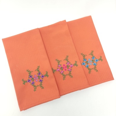 Três panos de tecido terracota com bordados florais coloridos