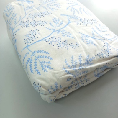 Cobertor dobrado branco com padrão azul de folhas e ramos