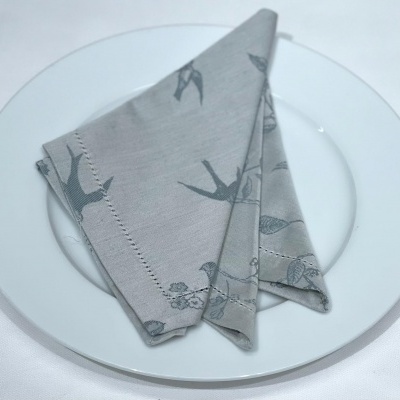 Guardanapo cinza com padrão de pássaros sobre prato branco