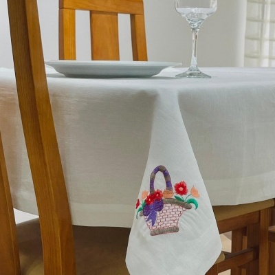 Toalha de mesa branca com bordado de cesta com flores, mesa de madeira com cadeiras, prato e copo