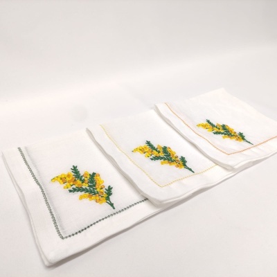Três toalhas brancas com bordados florais amarelos e folhas verdes, com bordas coloridas distintas.