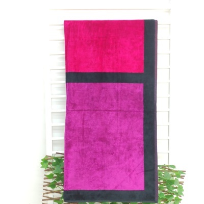 Toalha de banho rosa e roxa com bordas pretas pendurada num cabide branco