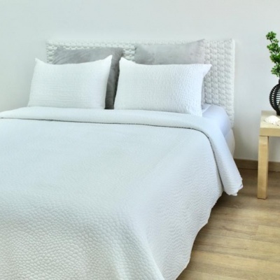 Cama de casal com edredão e almofadas brancas e mesa de cabeceira com vaso