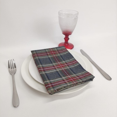 Conjunto de mesa com talheres metálicos, prato branco, guardanapo xadrez e copo transparente com base vermelha