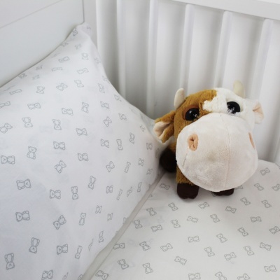Lençol e almofada brancos com padrão cinzento e peluche de vaca sobre o lençol num berço branco