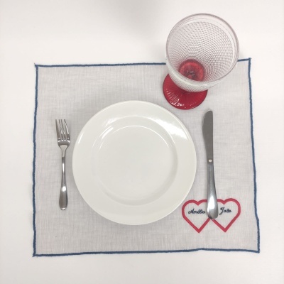 Conjunto de mesa com prato branco, talheres metálicos, individual bege com borda azul e copo com base vermelha