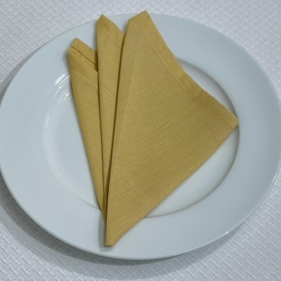 Guardanapo mostarda dobrado sobre prato branco numa mesa com toalha branca texturizada