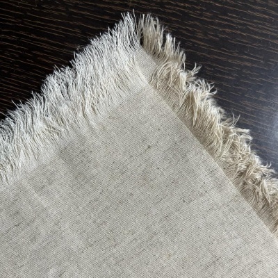 Toalha ou tecido creme com franjas sobre superfície escura de madeira