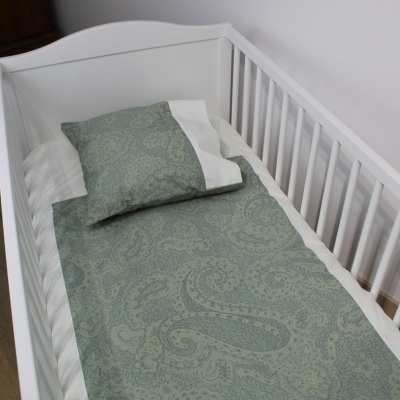 Berço branco com roupa de cama verde decorativa e parede branca ao fundo
