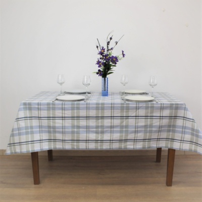 Mesa de madeira com toalha de mesa xadrez azul, pratos brancos e vaso azul com flores