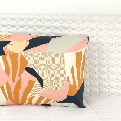 Travesseiro decorativo colorido com padrão geométrico sobre cama branca