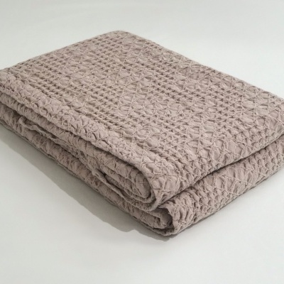 Manta dobrada com textura tipo waffle cor bege claro sobre superfície branca