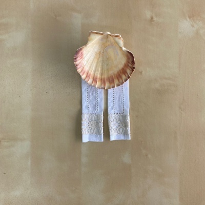 Concha marinha amarelo e rosa sobre dois tecidos brancos bordados em superfície bege