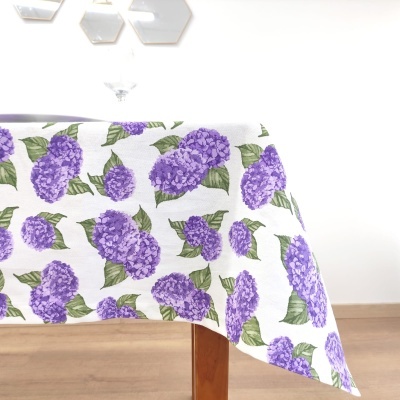 Toalha de mesa branca com flores roxas e folhas verdes numa mesa de madeira